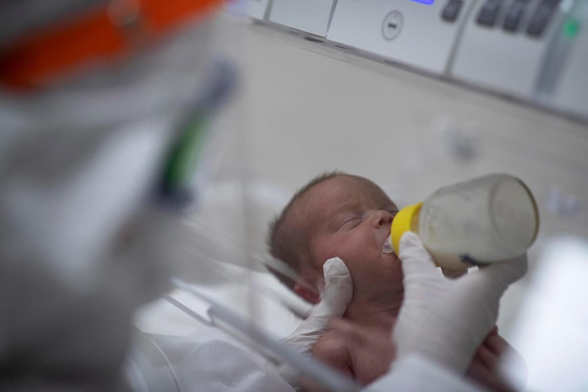 Un operatore sanitario, protetto da tuta, visiera e mascherina, dà da mangiare a un neonato il latte della mamma, positiva al coronavirus ??